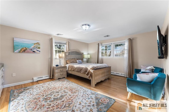 bedroom with a baseboard heating unit, multiple windows, and light wood-style flooring