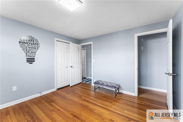 unfurnished bedroom featuring wood finished floors, baseboards, and a closet