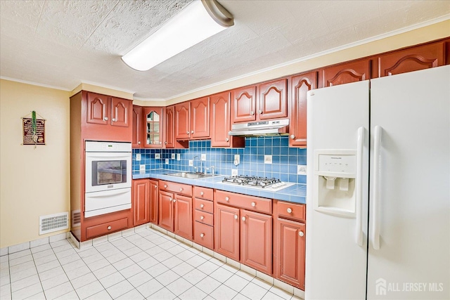 115 W Woodbridge Ave W, Iselin, NJ 08830 - kitchen with white appliances, a warming drawer, backsplash, under cabinet range hood, and tile counters