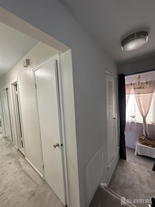 hallway featuring visible vents, light carpet, and an inviting chandelier