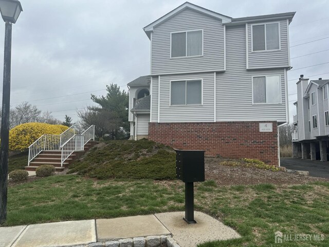 view of side of home with a yard, brick siding, and stairs