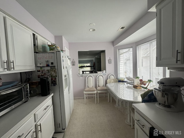 kitchen featuring light countertops, white fridge with ice dispenser, light floors, baseboards, and a toaster