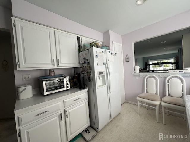 kitchen with a toaster, light countertops, baseboards, white cabinets, and white fridge with ice dispenser
