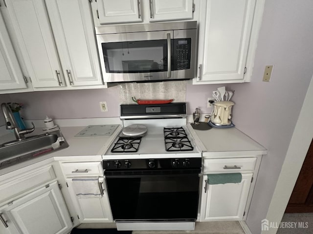 kitchen featuring light countertops, stainless steel microwave, white cabinetry, and gas range