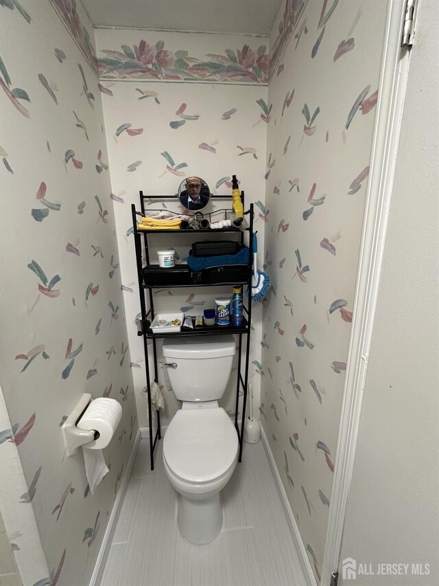 bathroom featuring baseboards, toilet, and wallpapered walls
