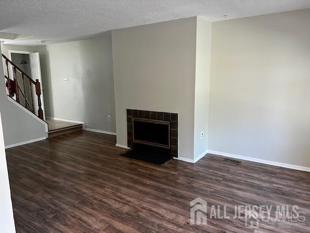 unfurnished living room with a tiled fireplace, dark hardwood / wood-style flooring, and a textured ceiling