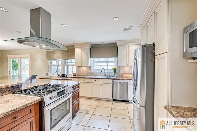 kitchen with stainless steel appliances, a sink, visible vents, island range hood, and decorative backsplash