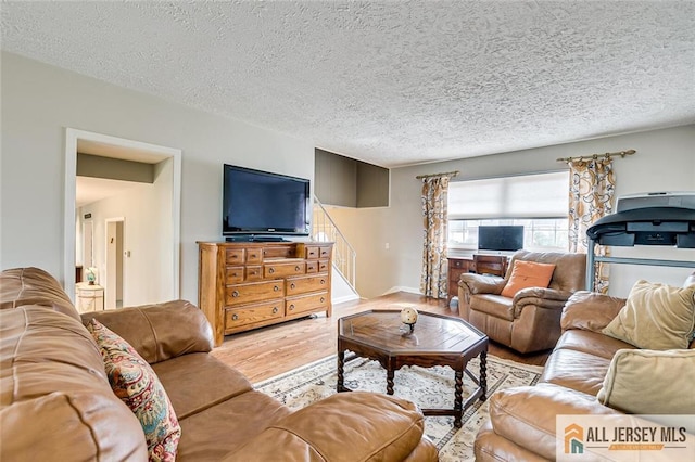 living area with baseboards, wood finished floors, a textured ceiling, and stairway