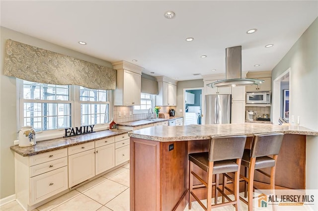 kitchen featuring a kitchen breakfast bar, a sink, decorative backsplash, stainless steel fridge, and white microwave