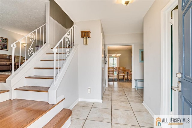 foyer entrance with baseboards, a notable chandelier, stairs, and light tile patterned flooring