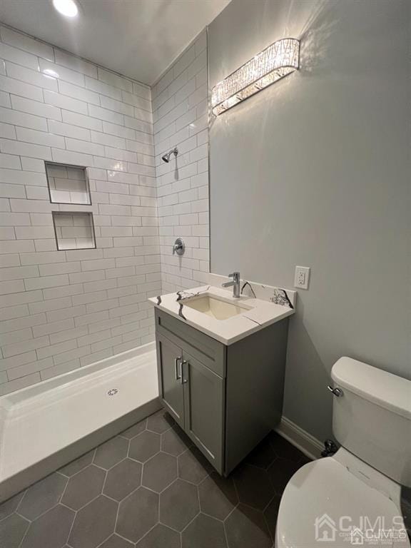 bathroom featuring vanity, tile patterned floors, a tile shower, and toilet