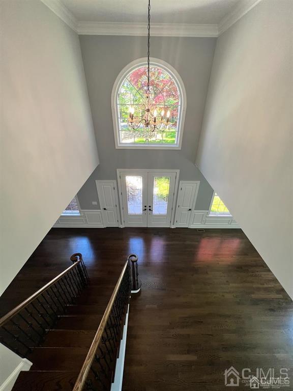 foyer entrance with a high ceiling, crown molding, an inviting chandelier, french doors, and dark wood-type flooring