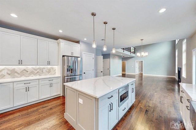 kitchen with backsplash, a kitchen island, stainless steel appliances, hardwood / wood-style floors, and decorative light fixtures