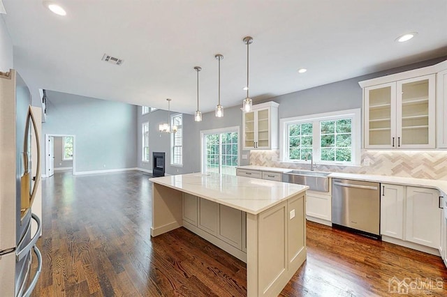 kitchen with tasteful backsplash, hanging light fixtures, dark hardwood / wood-style floors, a kitchen island, and appliances with stainless steel finishes