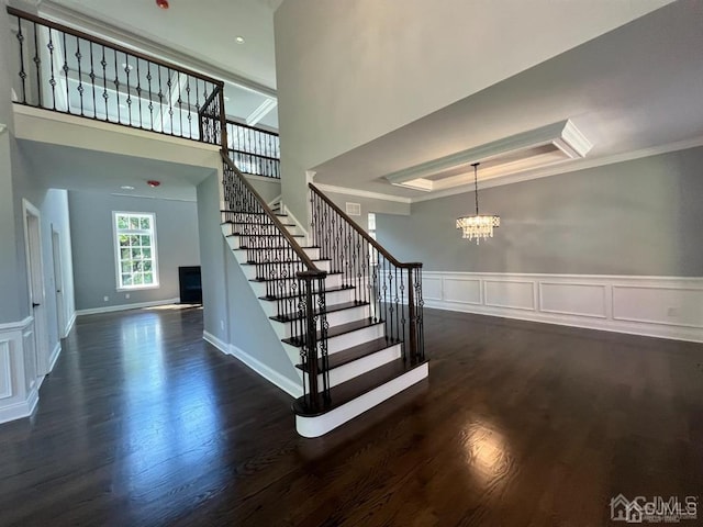 staircase featuring an inviting chandelier, dark hardwood / wood-style flooring, ornamental molding, and a towering ceiling