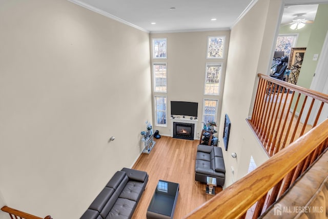 living area with wood finished floors, crown molding, a fireplace with flush hearth, recessed lighting, and ceiling fan