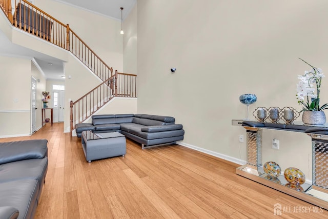 living room with light wood-style floors, baseboards, stairway, a high ceiling, and ornamental molding
