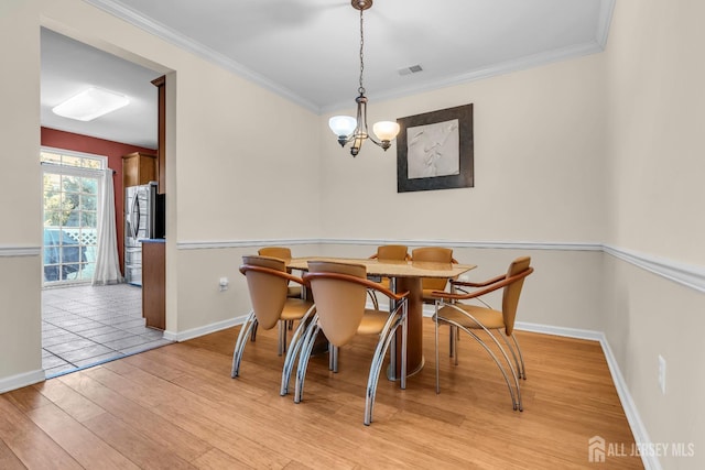 dining room with an inviting chandelier, ornamental molding, and light wood-type flooring