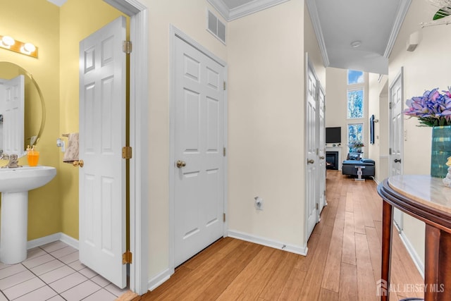 corridor featuring ornamental molding, baseboards, light wood-type flooring, and a sink