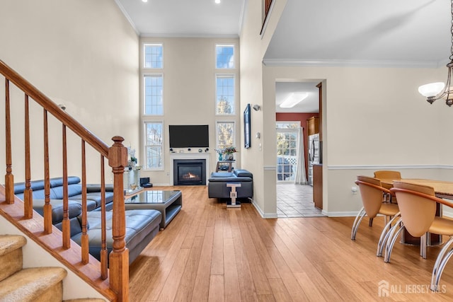 living area with stairs, a glass covered fireplace, ornamental molding, light wood-type flooring, and baseboards