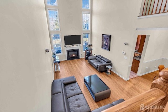 living room featuring a high ceiling, baseboards, wood finished floors, and a glass covered fireplace