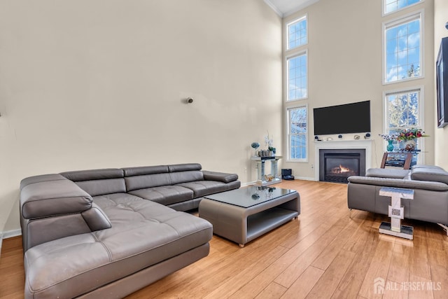 living room featuring a towering ceiling, wood finished floors, a glass covered fireplace, ornamental molding, and baseboards