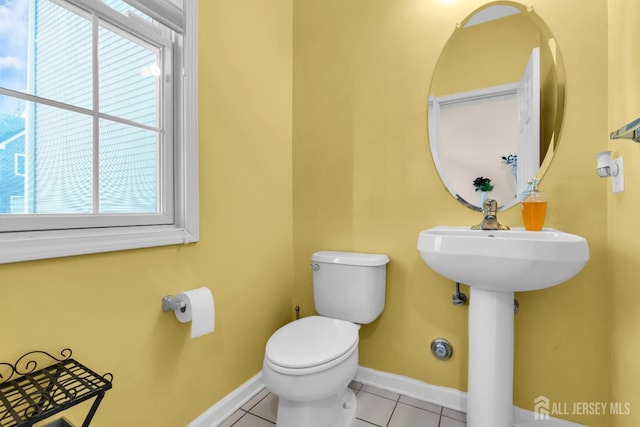 half bath featuring healthy amount of natural light, tile patterned flooring, toilet, and baseboards