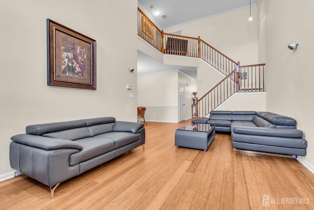 living room with light wood-style flooring, baseboards, stairs, a high ceiling, and ornamental molding