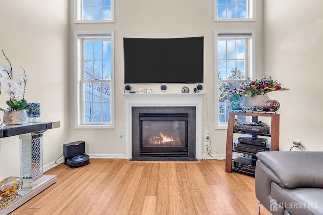living room with wood finished floors, a fireplace with flush hearth, plenty of natural light, and baseboards