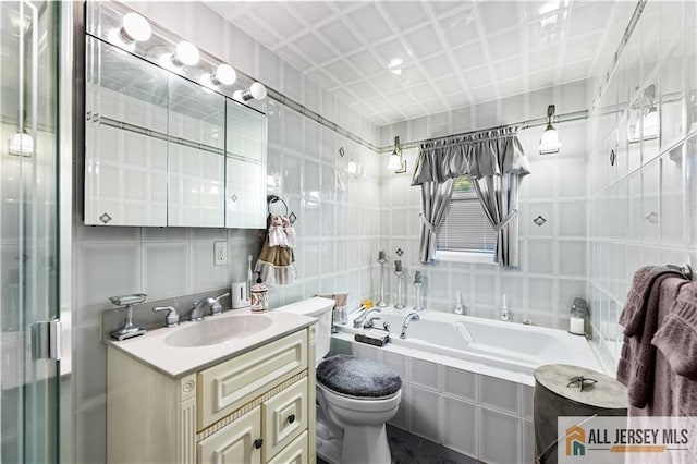 bathroom featuring vanity, a relaxing tiled tub, toilet, and tile walls