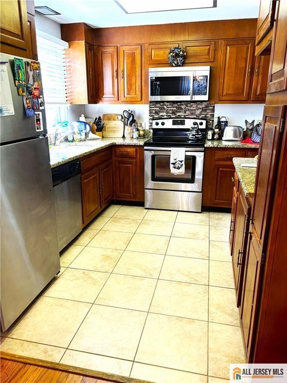 156 Pelham Ln Unit 156N, Monroe, NJ 08831 - kitchen featuring appliances with stainless steel finishes, light stone counters, and light tile patterned floors
