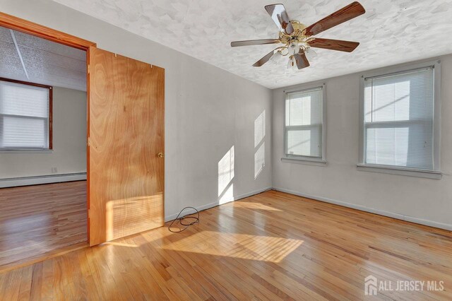 spare room featuring baseboard heating, light wood-type flooring, ceiling fan, and a textured ceiling