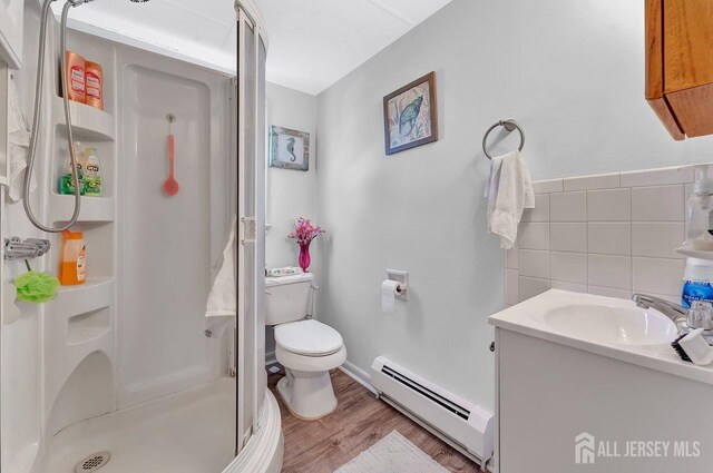 bathroom with vanity, tile walls, a shower with shower door, toilet, and a baseboard radiator