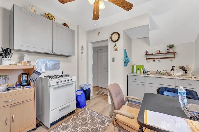 kitchen with sink, white gas range, light wood-type flooring, light stone countertops, and gray cabinetry