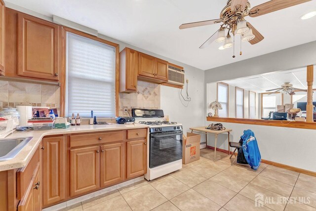 kitchen with a wall mounted AC, light tile patterned floors, ceiling fan, white gas range oven, and backsplash