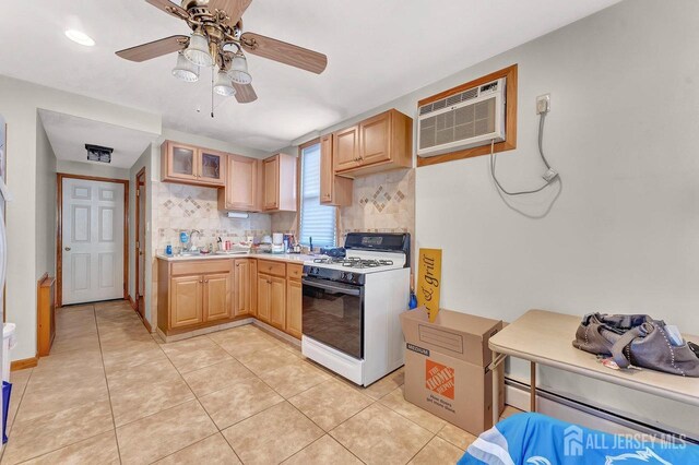 kitchen featuring an AC wall unit, white gas range oven, ceiling fan, light brown cabinetry, and backsplash