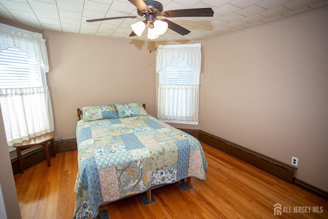 bedroom featuring hardwood / wood-style floors, a baseboard radiator, and ceiling fan