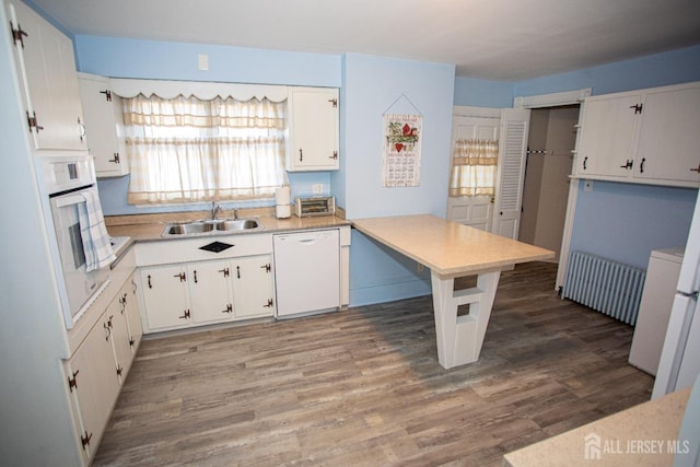 kitchen featuring radiator, white cabinetry, sink, and white appliances