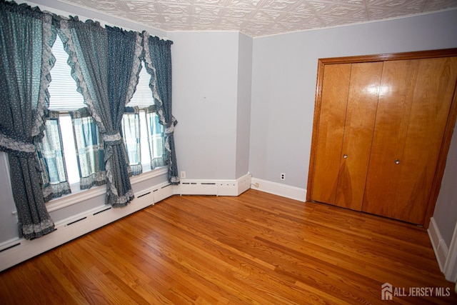 unfurnished bedroom featuring wood-type flooring, baseboard heating, and a closet