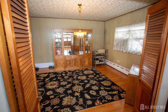 dining area with ornamental molding, hardwood / wood-style flooring, and a baseboard heating unit