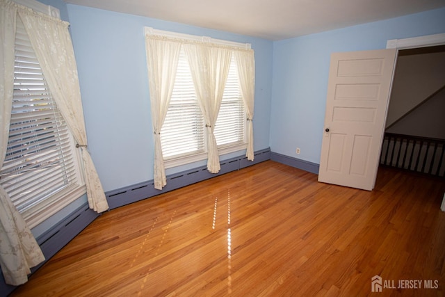 empty room with plenty of natural light, wood-type flooring, and a baseboard radiator