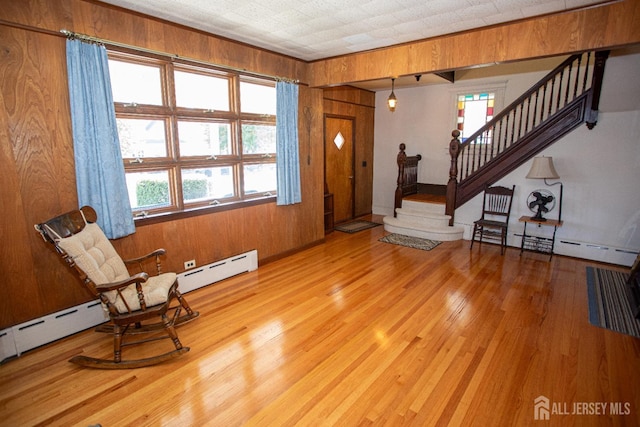 living area with wood walls, a healthy amount of sunlight, a baseboard radiator, and light wood-type flooring