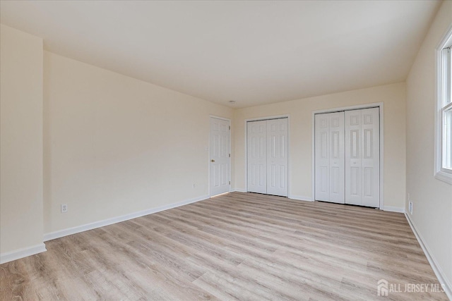 unfurnished bedroom with baseboards, two closets, and light wood-style flooring