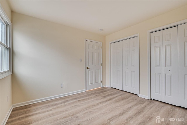 unfurnished bedroom with light wood-style flooring, baseboards, and multiple closets