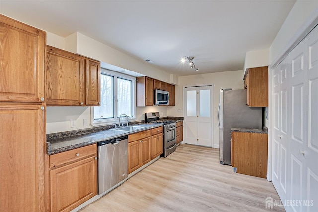 kitchen featuring dark countertops, light wood-type flooring, brown cabinetry, stainless steel appliances, and a sink