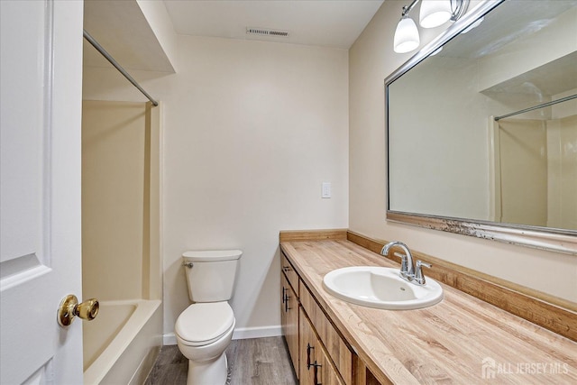 bathroom featuring visible vents, baseboards, toilet, wood finished floors, and vanity