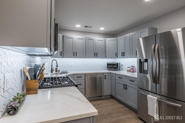 kitchen featuring decorative backsplash, light stone counters, gray cabinets, and stainless steel appliances