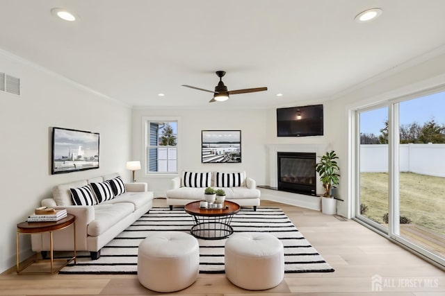 living room with light wood finished floors, plenty of natural light, visible vents, and ornamental molding