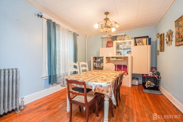 dining room featuring baseboards, radiator heating unit, ornamental molding, an inviting chandelier, and light wood-style floors