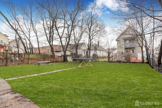 view of yard with a trampoline, fence, and a residential view